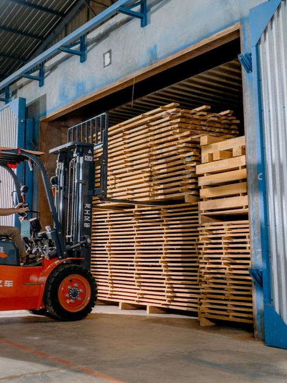 Wózek widłowy transportujący stosy drewnianych palet i desek w magazynie